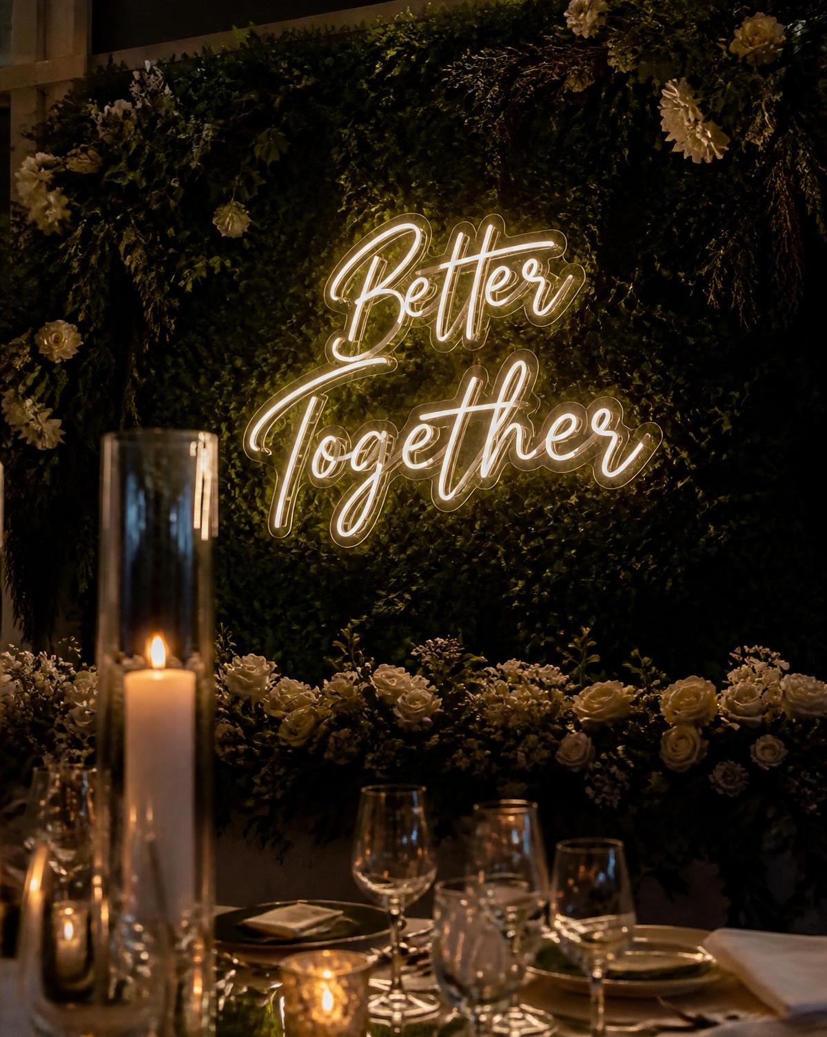 Warm white neon sign reading Better Together on a greenery wedding wall